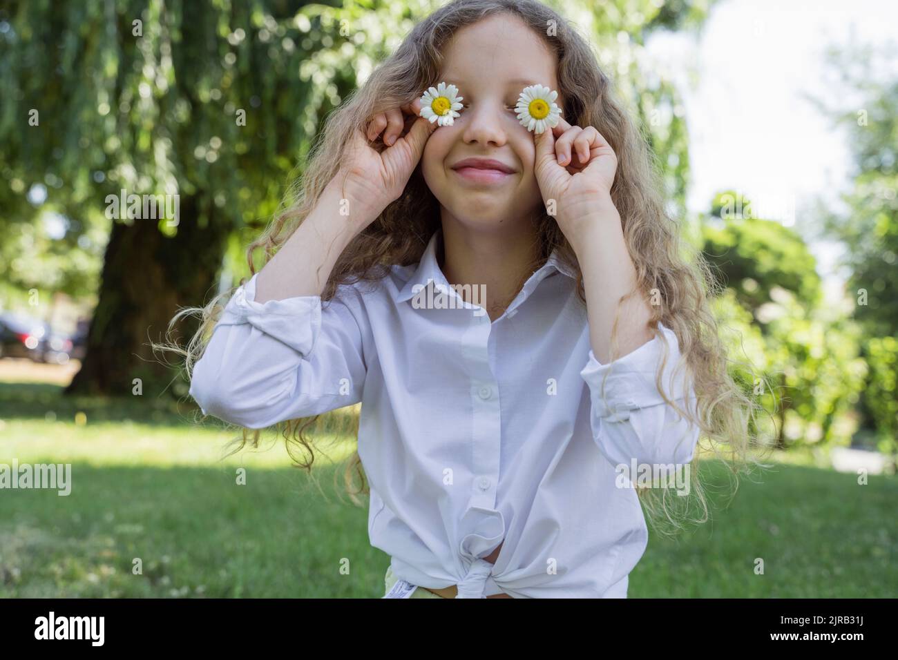 Smiling girl covering eyes with chamomile flowers Stock Photo - Alamy