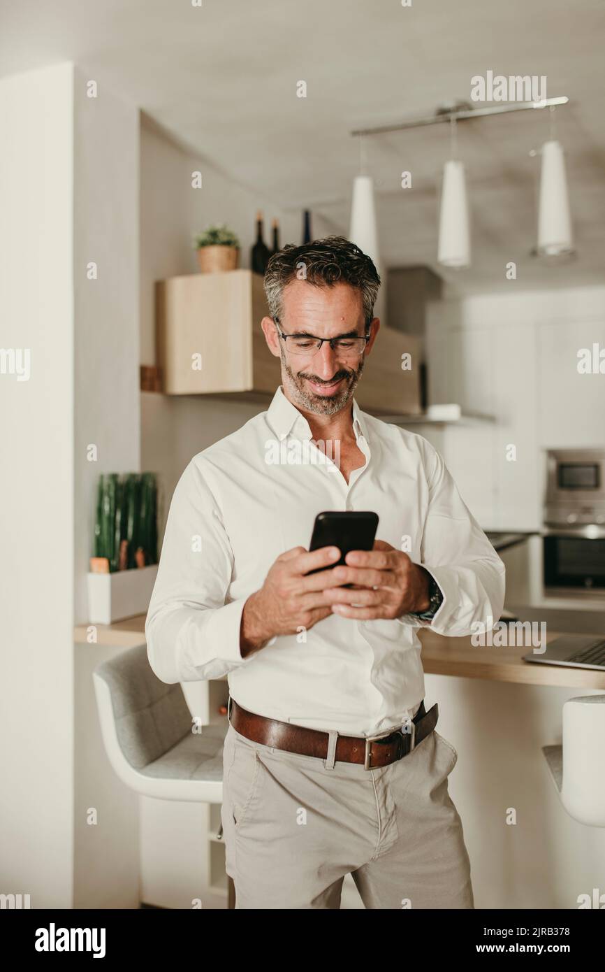 Smiling businessman using mobile phone at home Stock Photo
