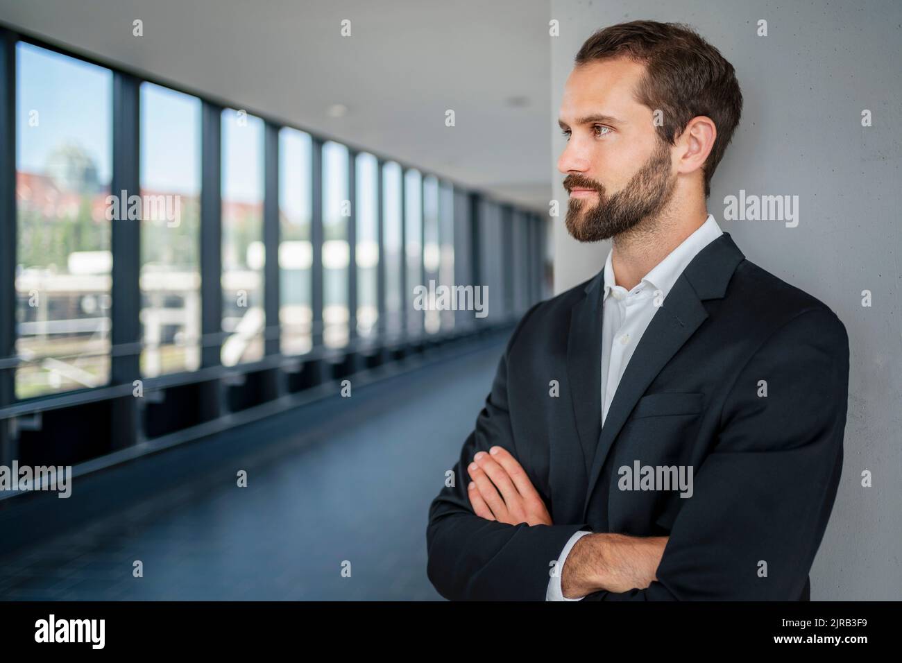 Contemplative businessman with arms crossed standing in front of wall ...