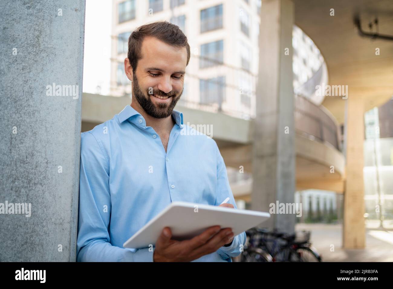 Smiling young businessman using tablet PC standing under bridge Stock Photo