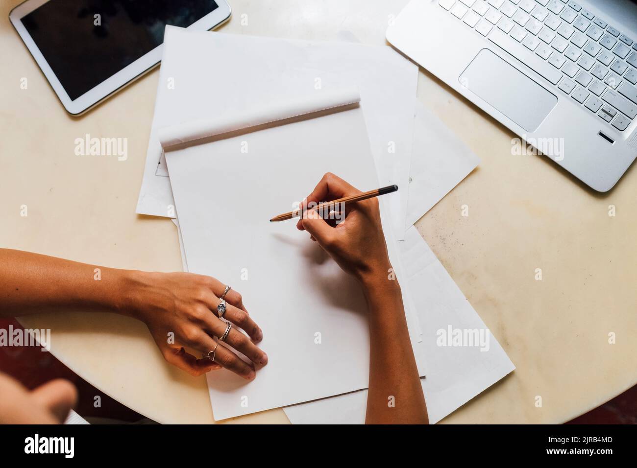 Hand of fashion designer holding pencil on sketch pad at desk Stock Photo
