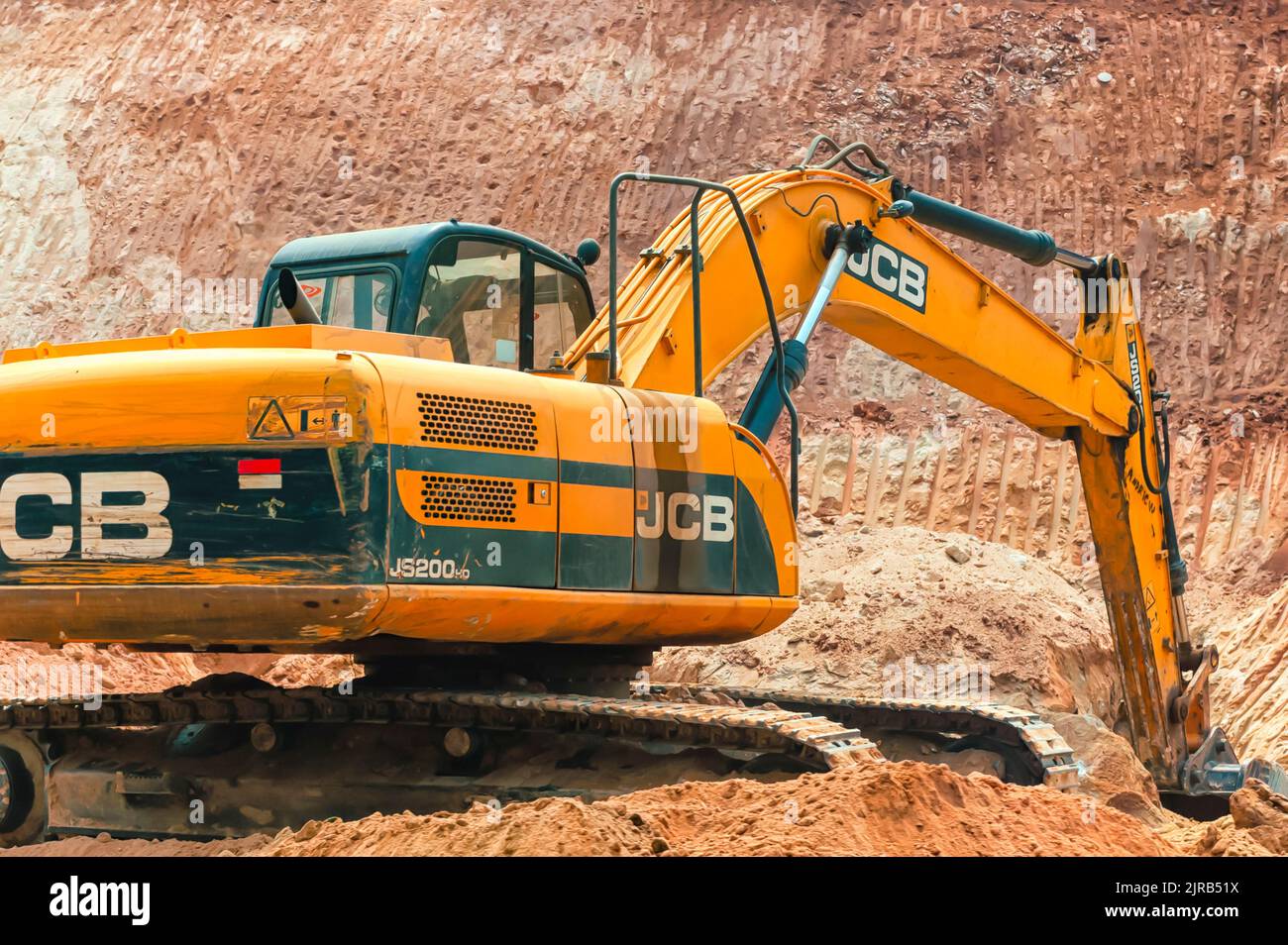 A JCB bulldozer / backhoe loader / dozer / crawler excavating huge volumes of sand while involved in a road building activity in India. Stock Photo