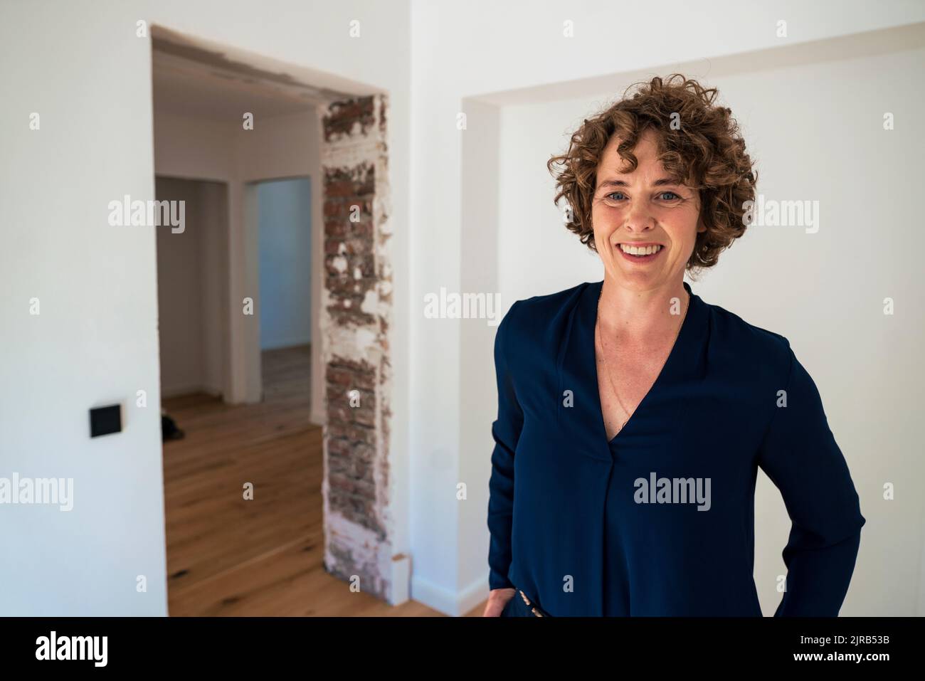 Smiling mature real estate agent with curly hair standing in new home ...