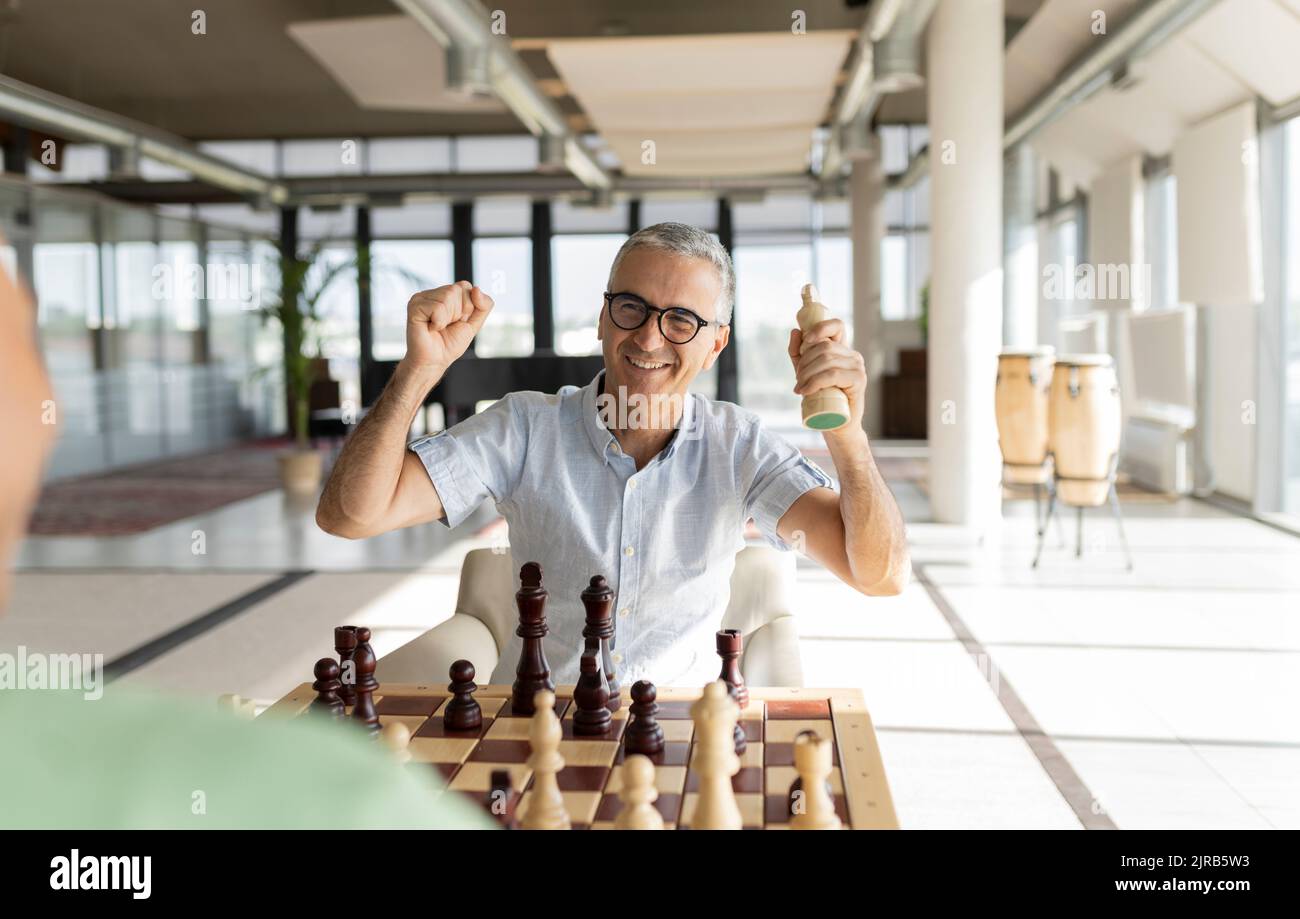 Happy businessman clenching fists with chess piece in office Stock Photo