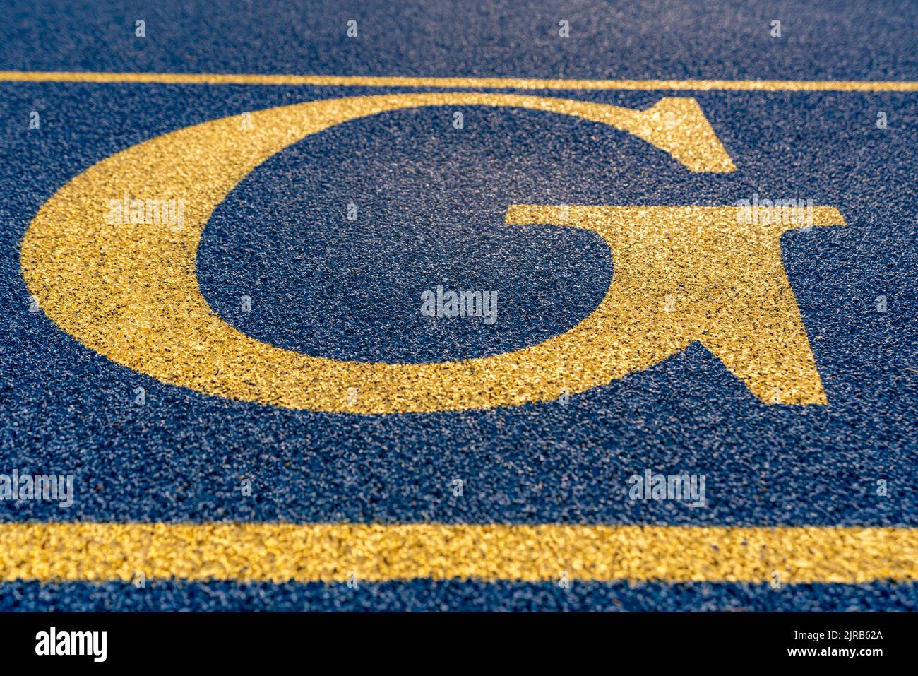 Close up the letter, initial G on a new blue running track with yellow lane lines. Stock Photo