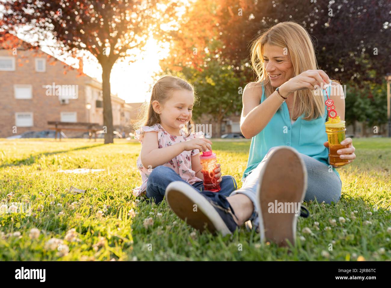 Smiling mother and daughter dipping bubble wands in bottles at park Stock Photo