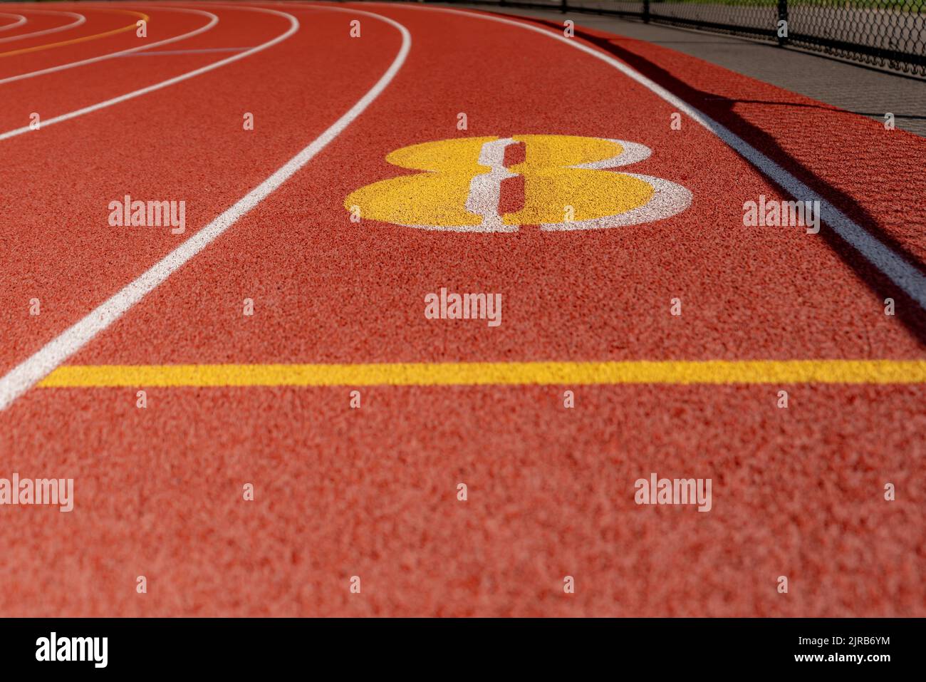 Close up lane number 8 on a new red running track with white lane lines and other markings Stock