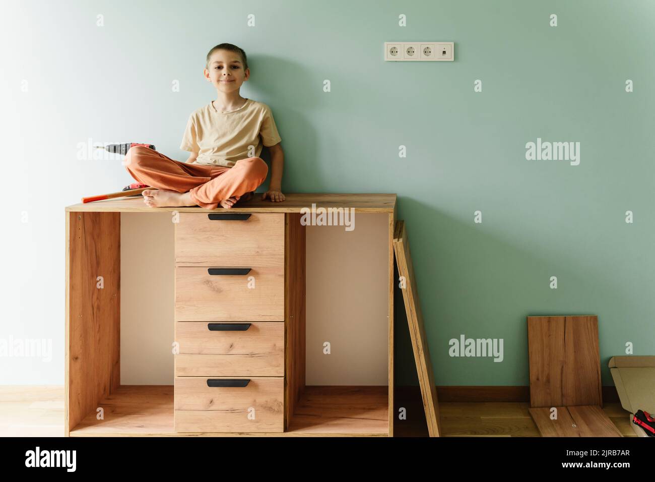 Smiling boy sitting on cabinet in front of wall at home Stock Photo