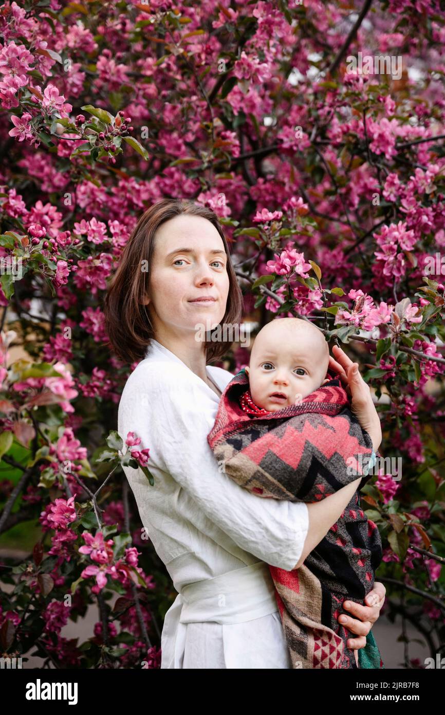 Smiling woman with baby boy standing in front of apple blossom tree Stock Photo