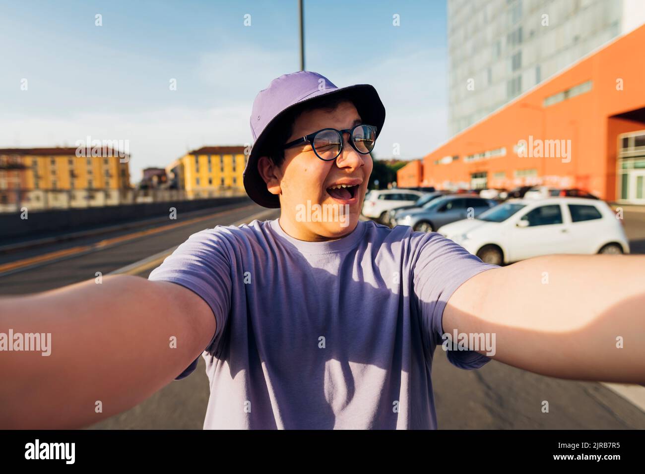Teenage boy winking and taking selfie at street on sunny day Stock Photo