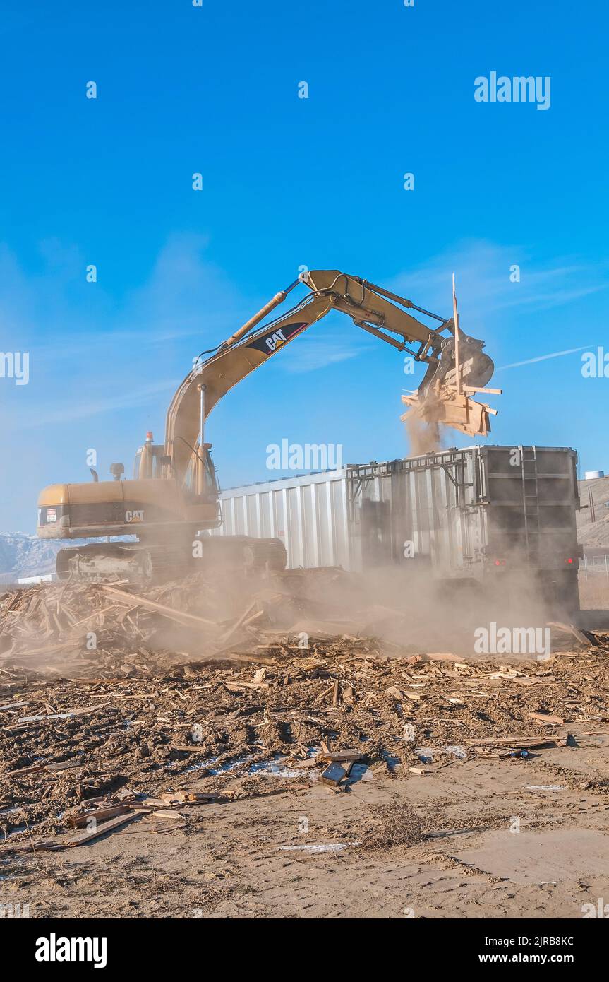 A power shovel loads solid waste into a large truck container for transport kicking up lots of dust in an active landfill. Stock Photo