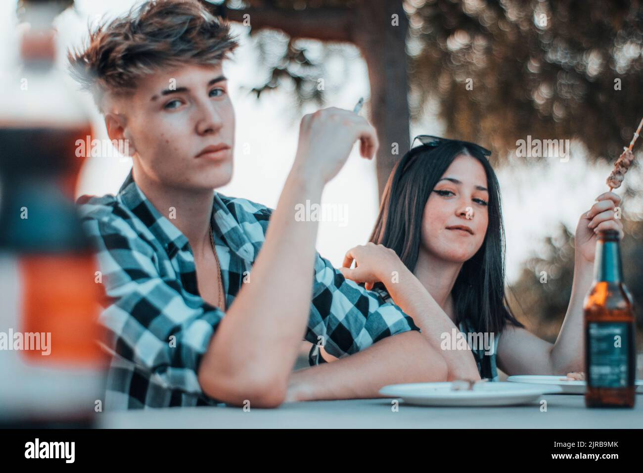 A shallow focus shot of a cute couple sitting near the table with a male  smoking a cigarette Stock Photo