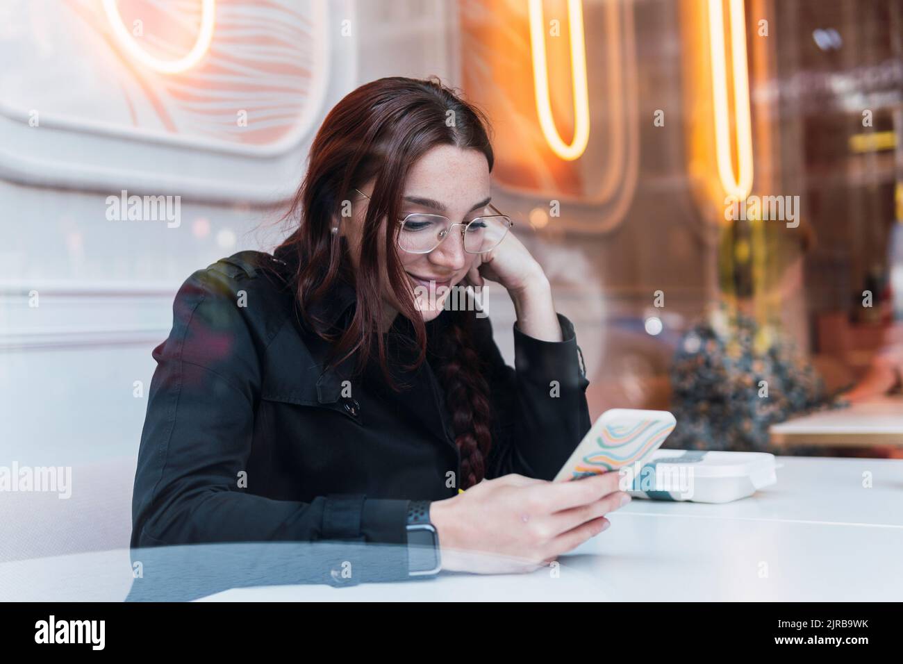 Smiling young woman using smart phone sitting at cafe Stock Photo