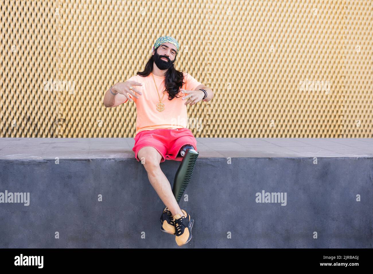 Bearded man with prosthetic leg sitting on wall Stock Photo
