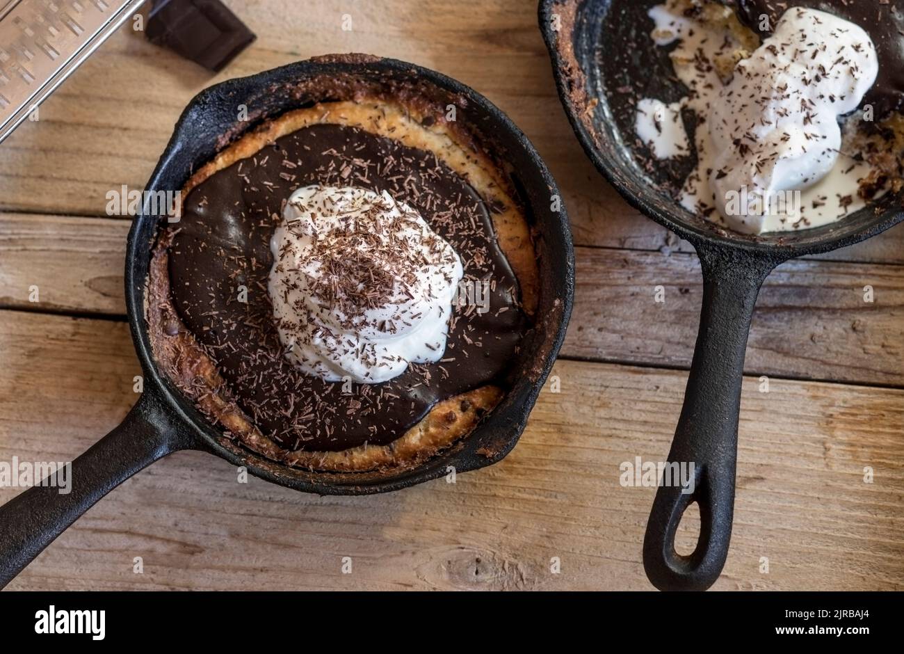 Frying pans with chocolate chip cookies covered with ganache topping and whipped cream Stock Photo