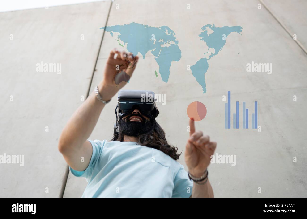 Smiling bearded man wearing VR glasses touching maps and chart Stock Photo