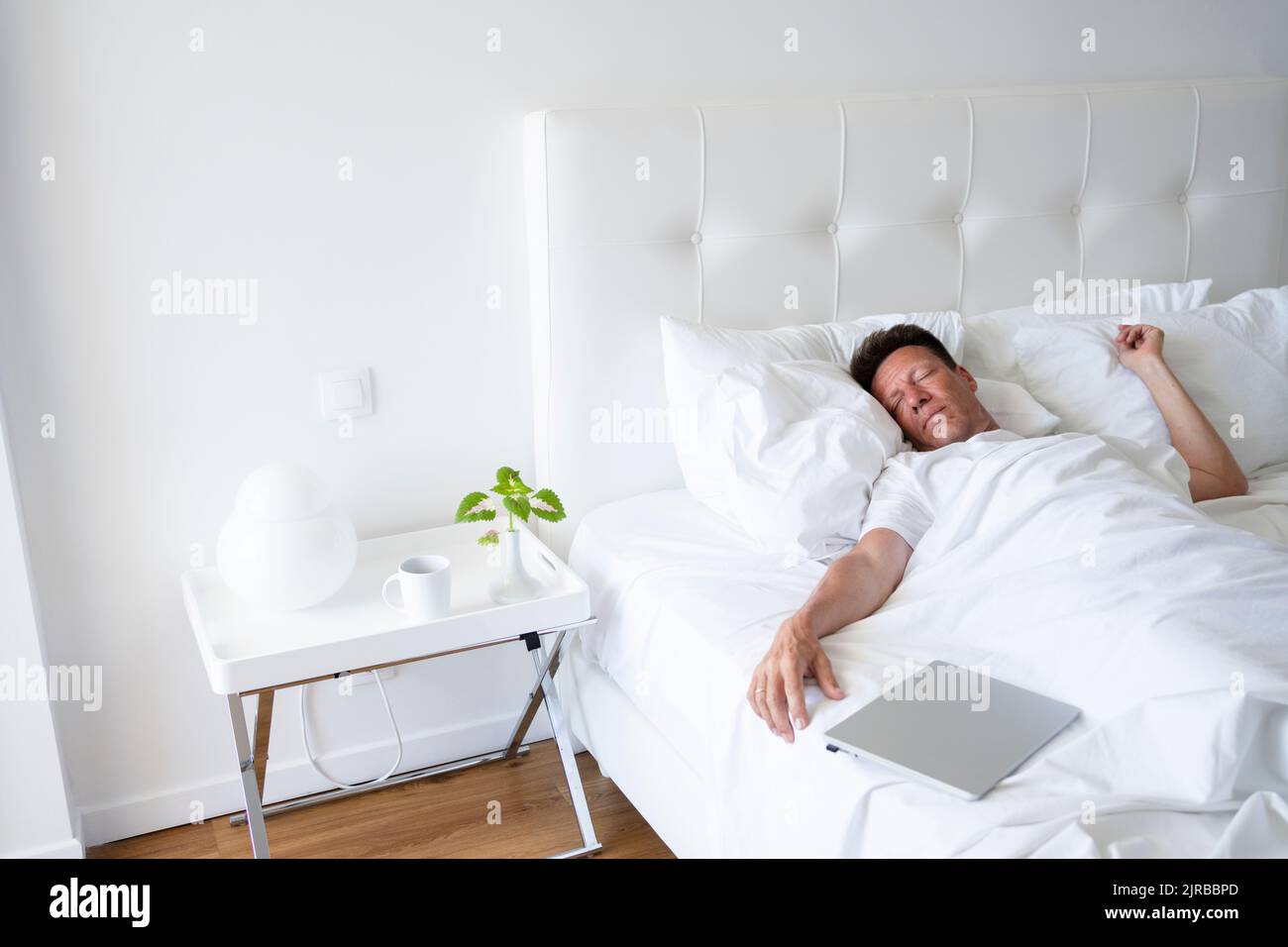 Mature man sleeping by laptop in bed Stock Photo