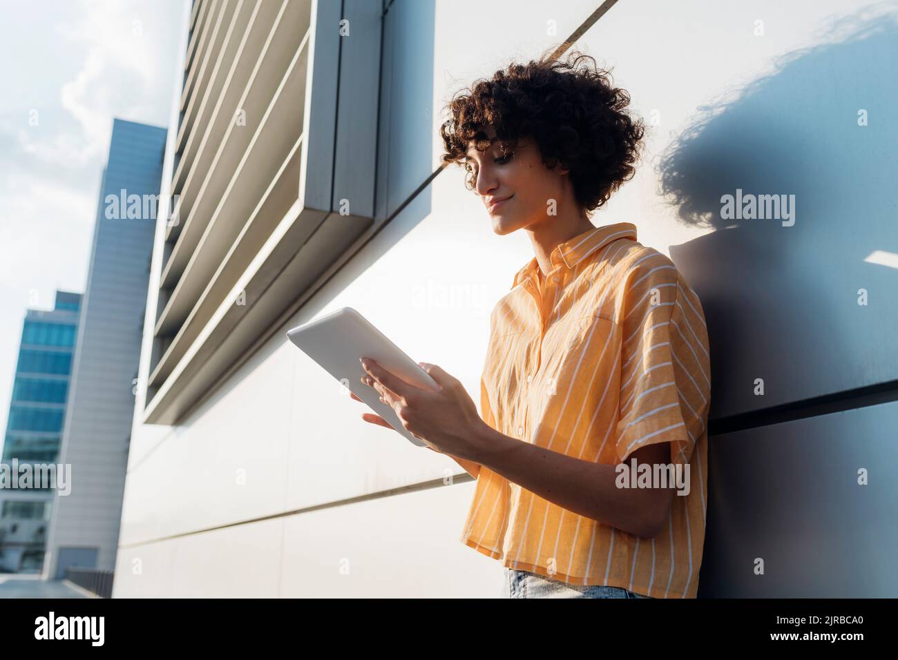 Smiling young freelancer using tablet PC by wall Stock Photo