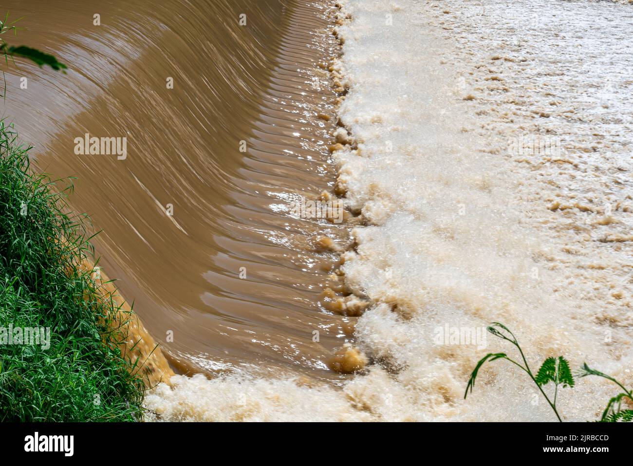 Fast moving muddy water rapids  over a weir and falling down splashing, foaming on a river. Stock Photo