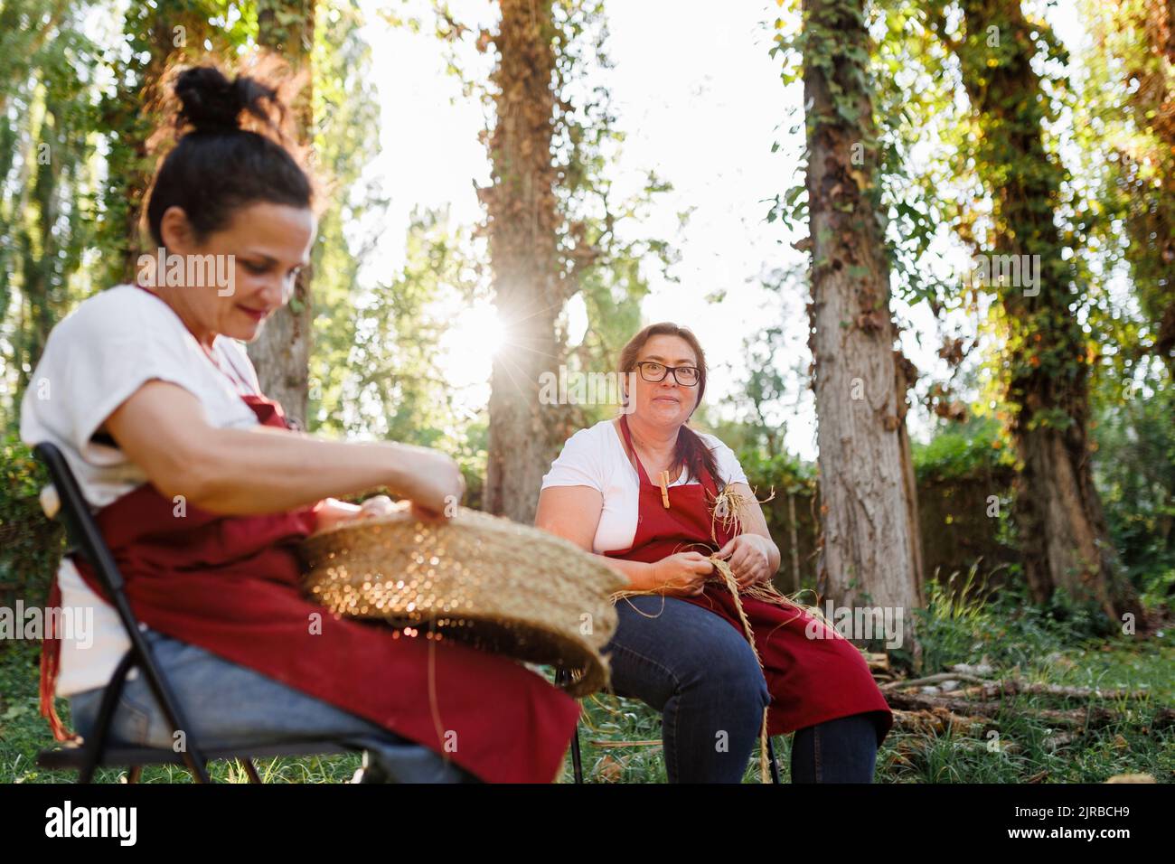 Smiling artisan with coworker weaving esparto grass in garden Stock