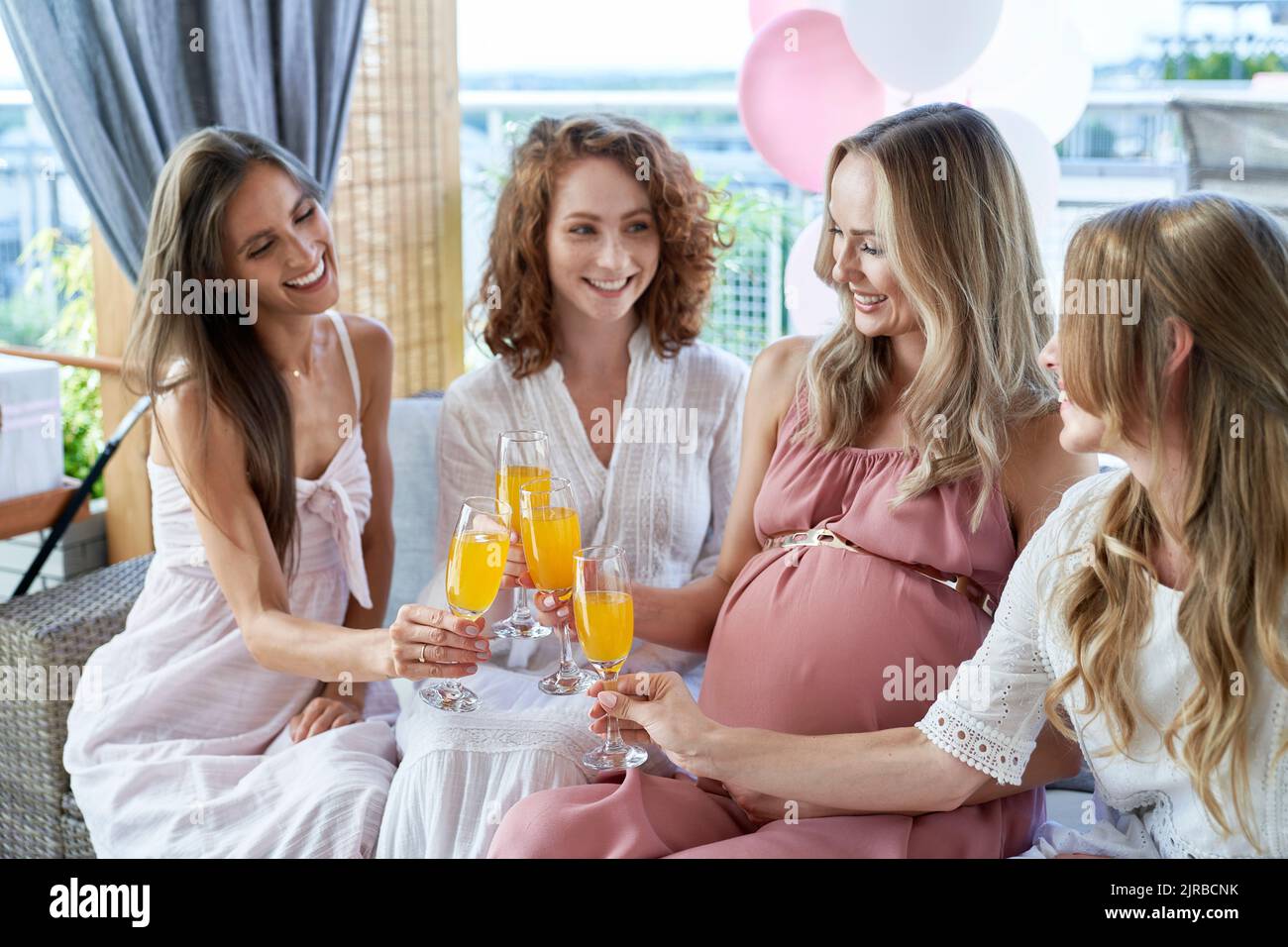 Smiling pregnant woman toasting cocktail glasses with friends Stock