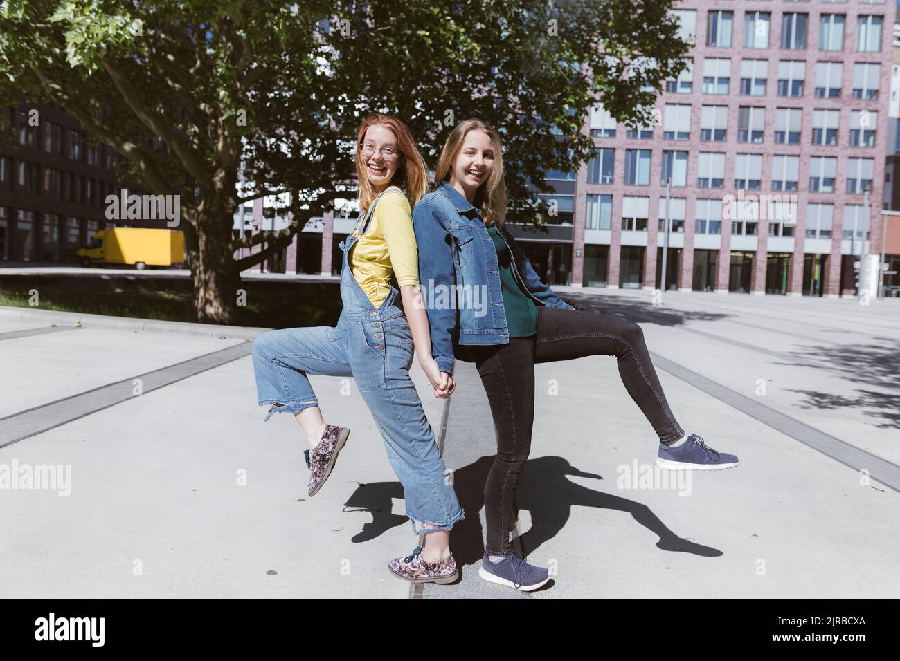 Playful young friends standing back to back on one leg Stock Photo