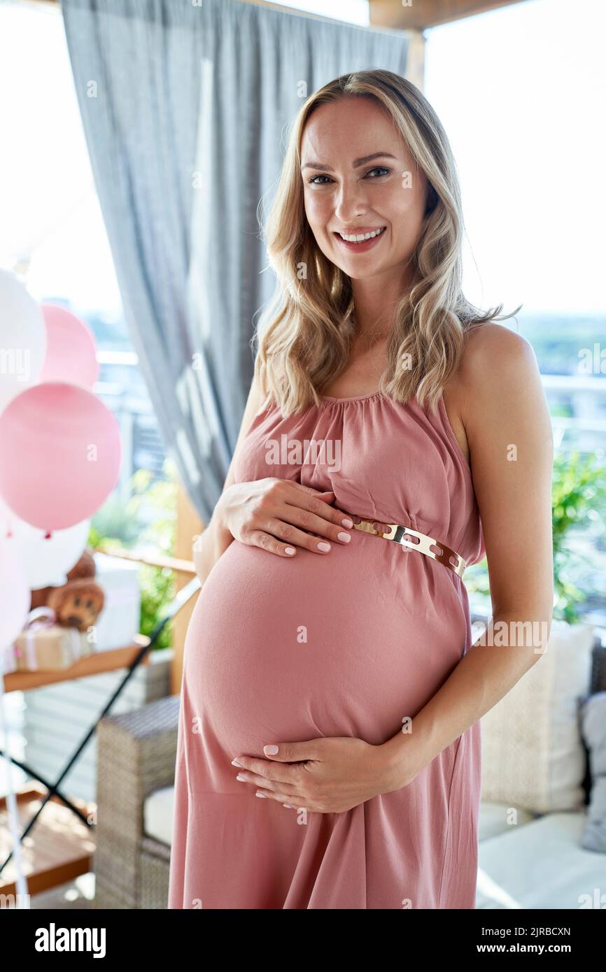 Happy pregnant woman wearing pink dress at baby shower Stock Photo