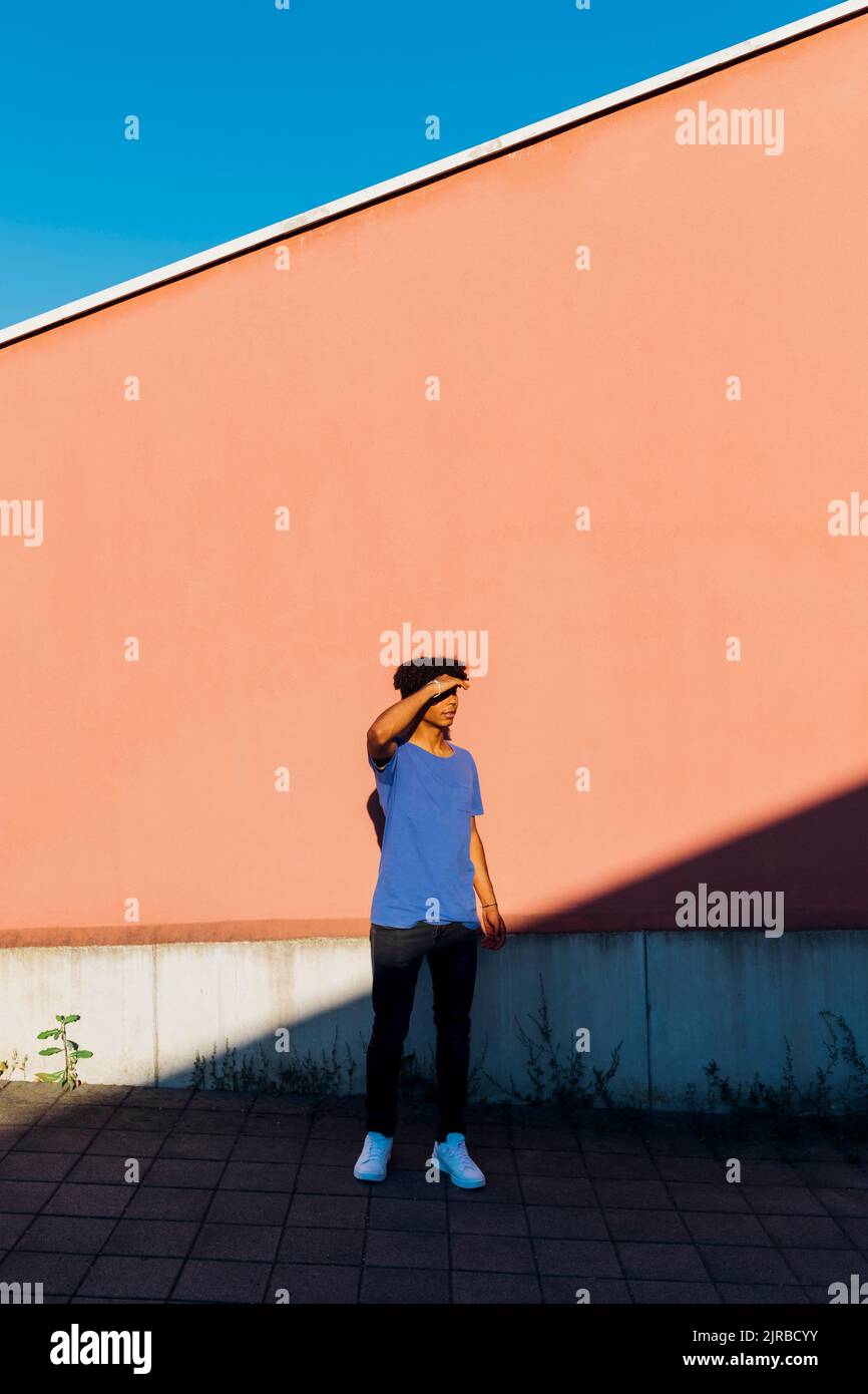 Young man shielding eyes standing in front of wall Stock Photo - Alamy
