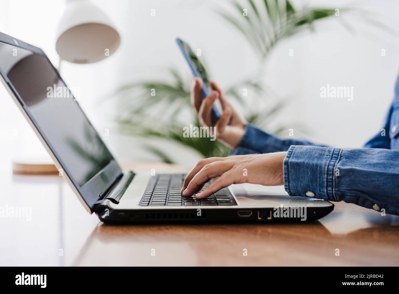 Freelancer using laptop holding smart phone at home office Stock Photo