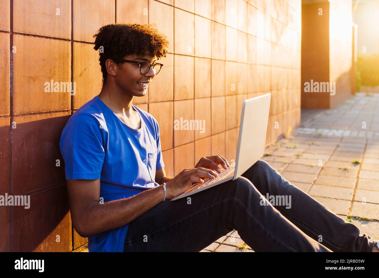 Smiling man using laptop for studying sitting by wall Stock Photo
