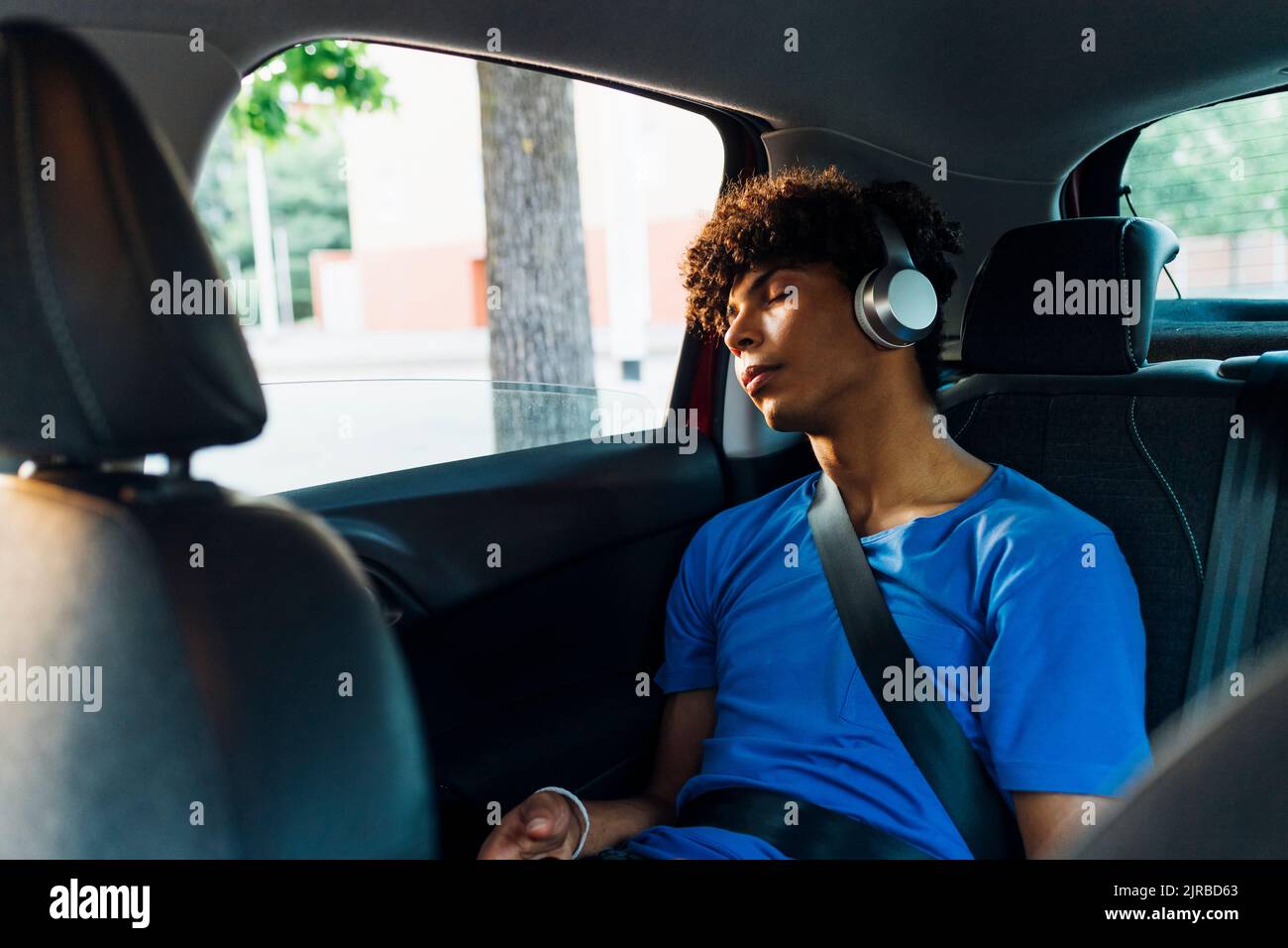 Tired young man wearing wireless headphones sleeping in car on road trip Stock Photo