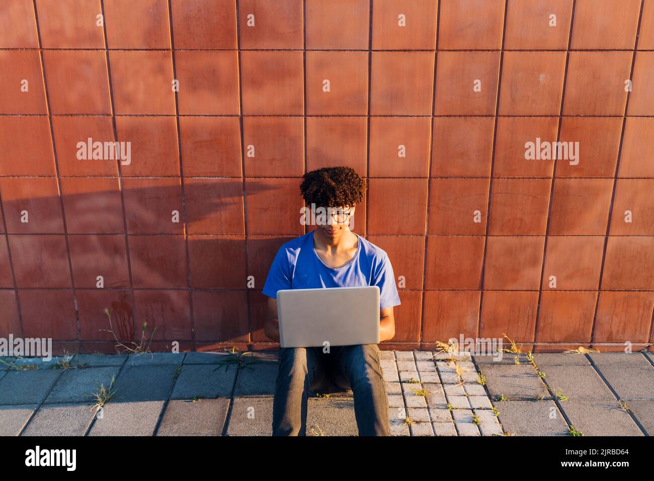 Young man using laptop for studying sitting leaning on wall Stock Photo