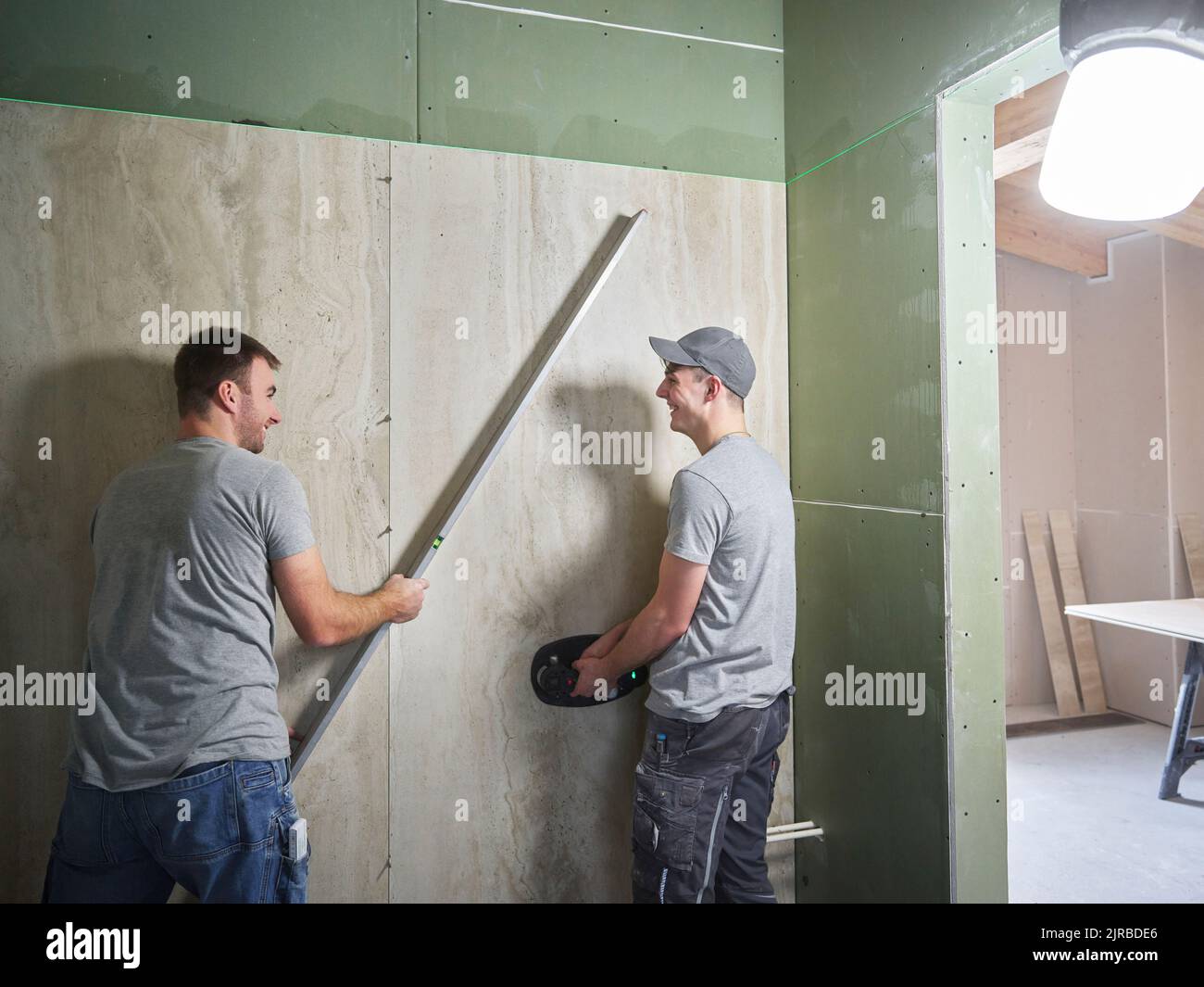 Happy tilers lifting large ceramic tiles onto wall with vacuum suction