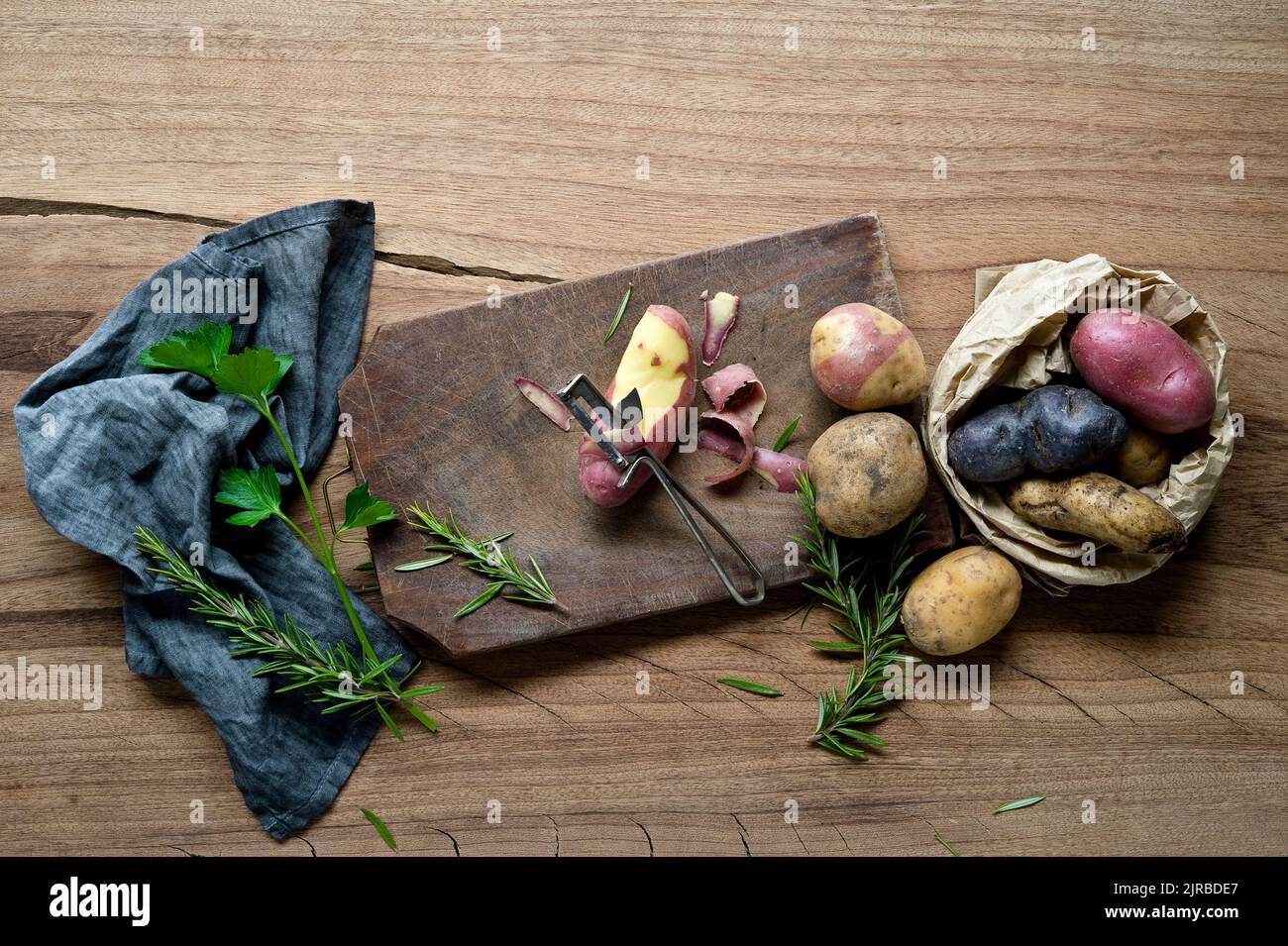 https://c8.alamy.com/comp/2JRBDE7/herbs-dish-towel-cutting-board-potato-peeler-and-different-varieties-of-raw-potatoes-2JRBDE7.jpg