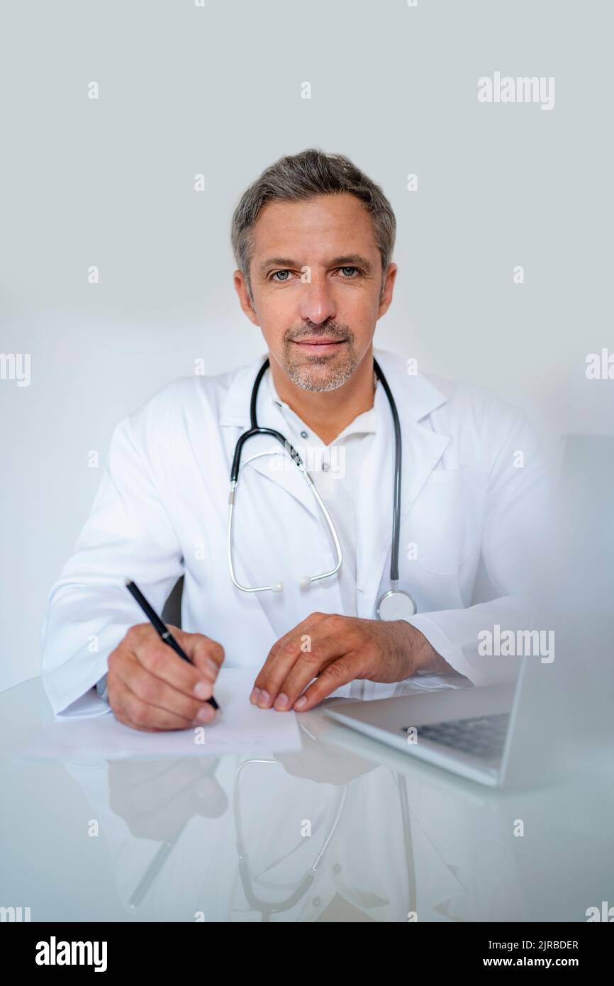 Portrait of mature doctor sitting at desk in medical practice Stock
