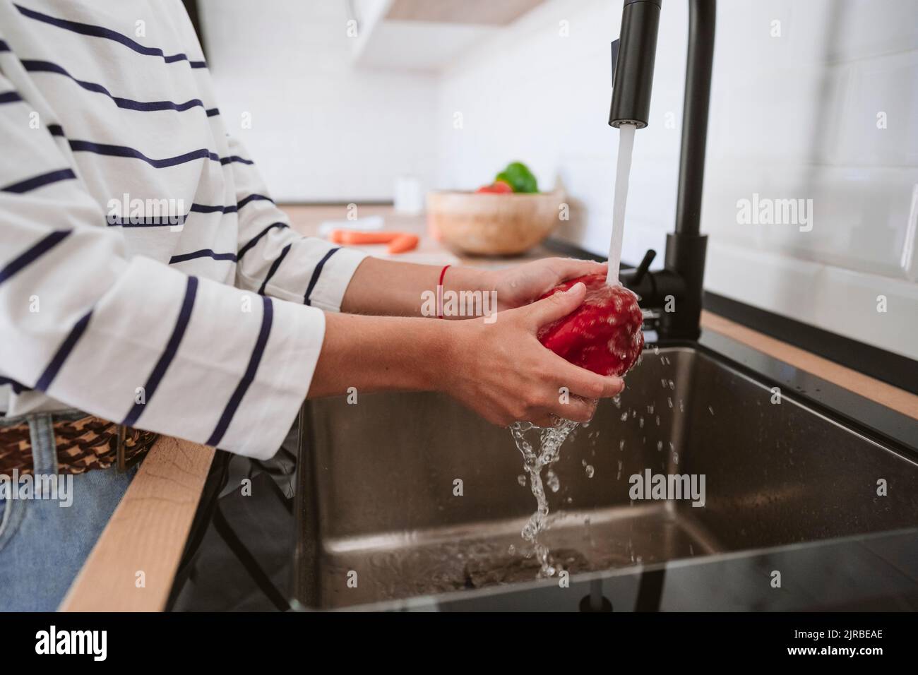 Woman washing bell pepper in kitchen at home Stock Photo