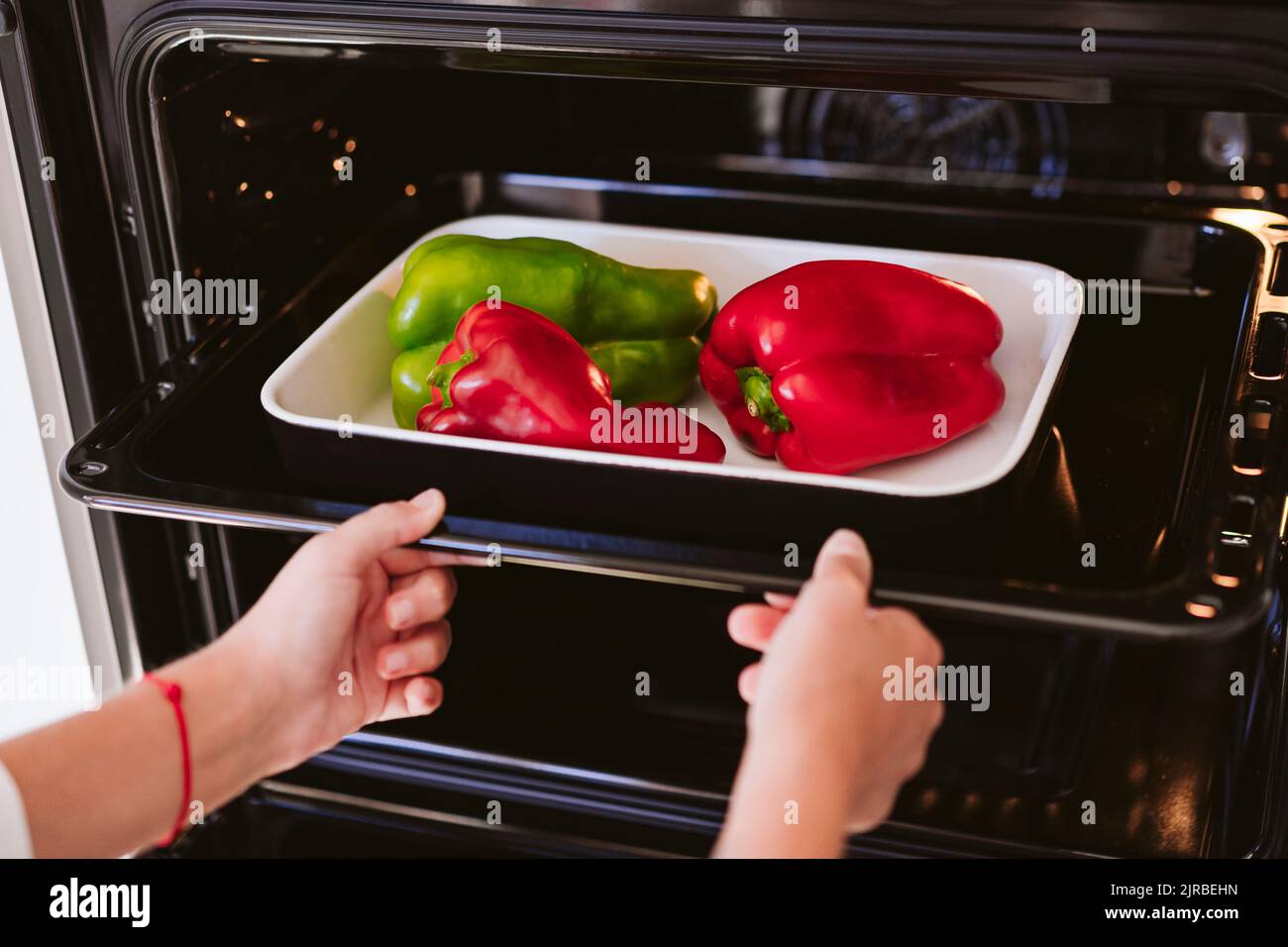 Woman putting bell peppers in oven at home Stock Photo Alamy