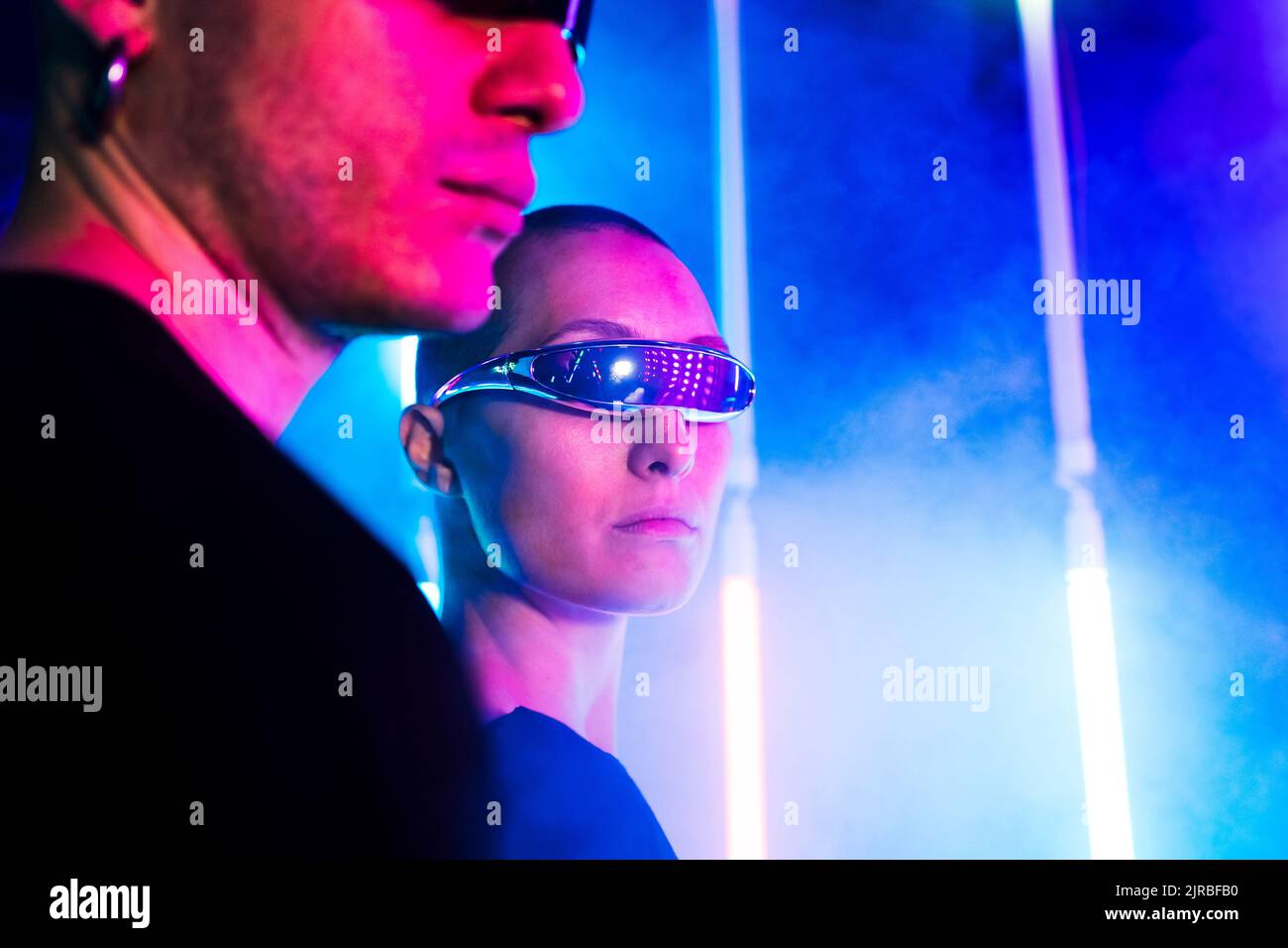 Young woman wearing futuristic glasses by man near illuminated background Stock Photo