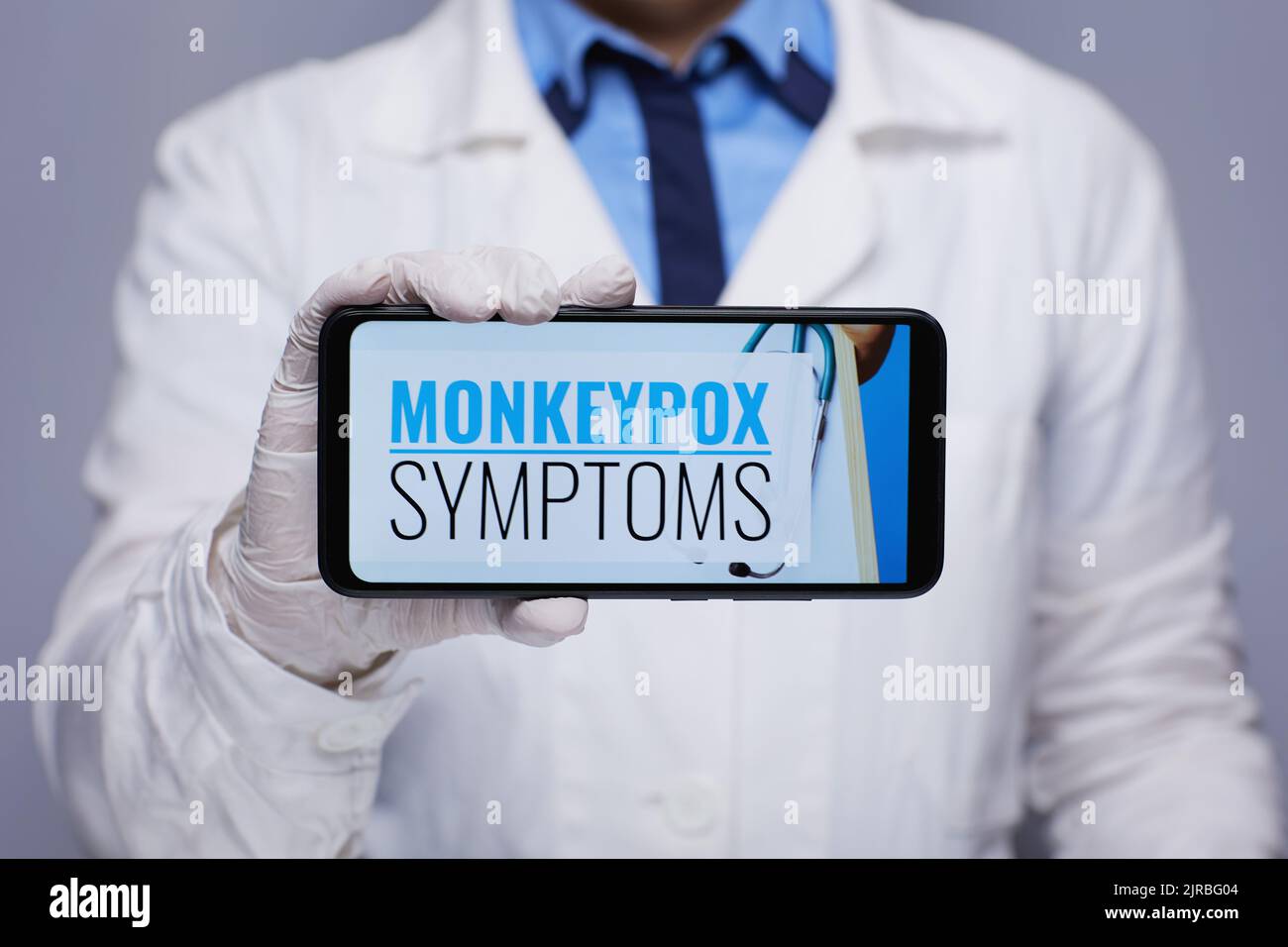 Closeup on modern female medical doctor in white medical robe showing smartphone with monkeypox symptoms screen against grey background. Stock Photo