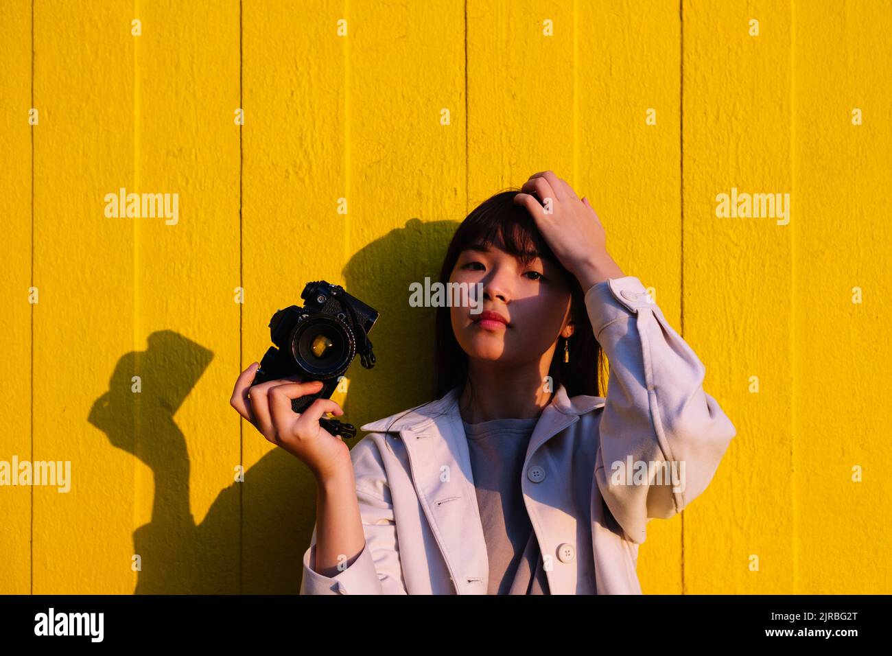 Young woman holding camera standing in front of wall Stock Photo - Alamy