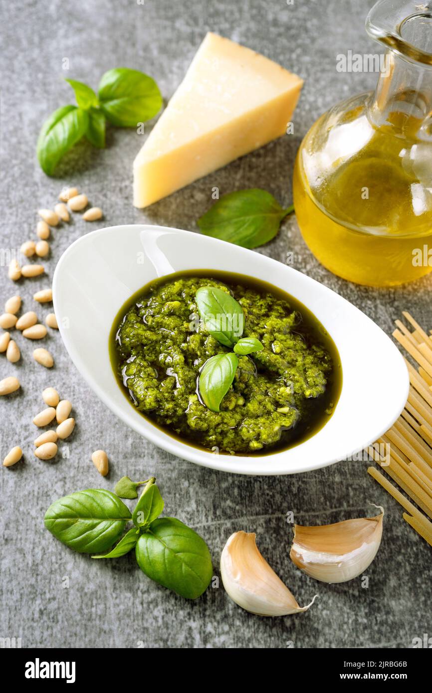 Homemade pesto sauce with ingredients. Sauce pesto in white bowl with basil, olive oil, pine nuts and parmesan cheese on gray concrete background Stock Photo