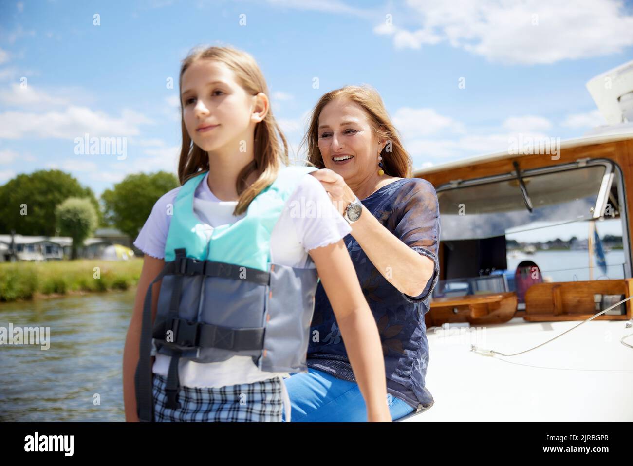 Grandmother helping granddaughter to wear life jacket on boat Stock