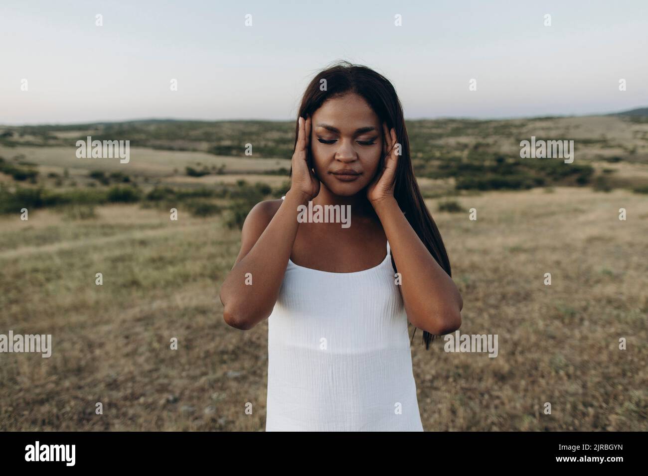 Woman with eyes closed rubbing head in meadow Stock Photo - Alamy
