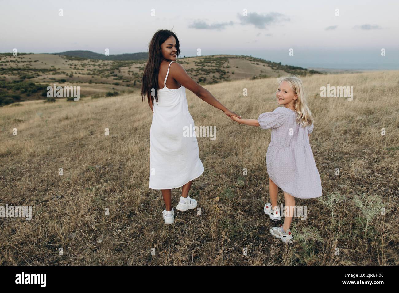 Smiling woman and girl holding hands walking in meadow Stock Photo