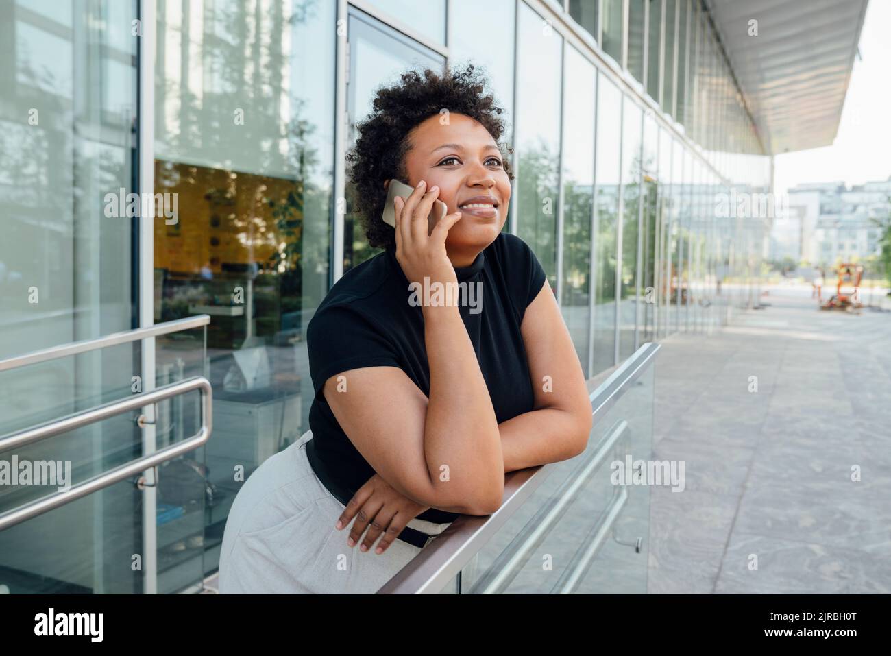 Smiling businesswoman talking on mobile phone leaning on railing Stock Photo