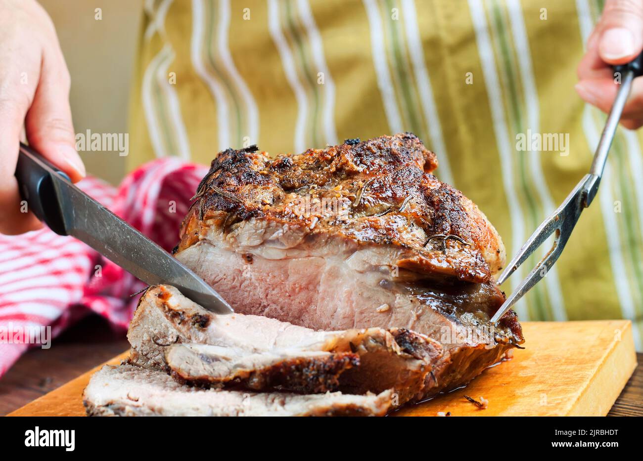Baked pork meat with spices sliced on brown cutting board with knife