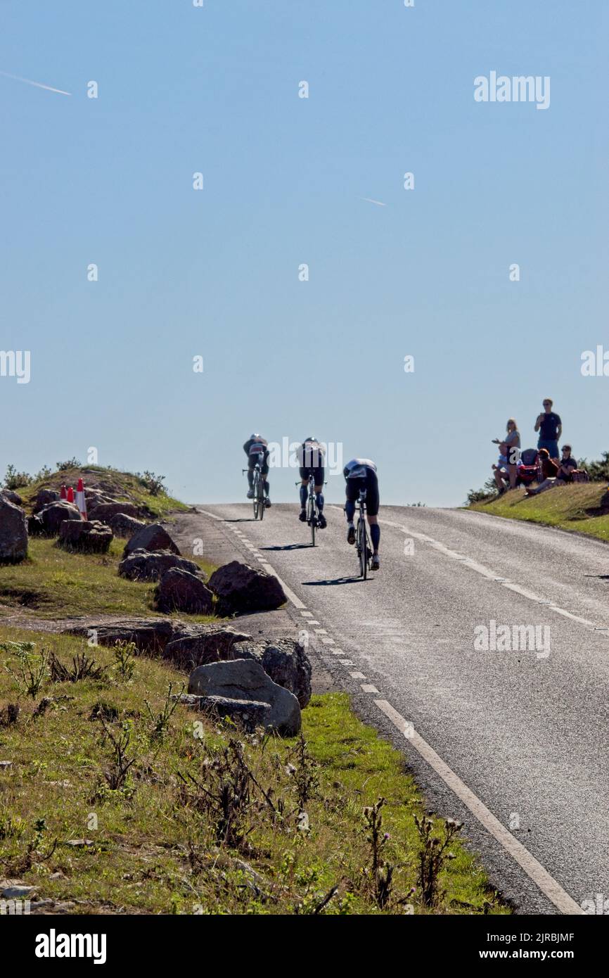 7thAug22 Gower Swansea Wales UK Triathlon Ironman cycling event Trio of cyclists heading uphill away from camera Two spectators in view at roadside Stock Photo
