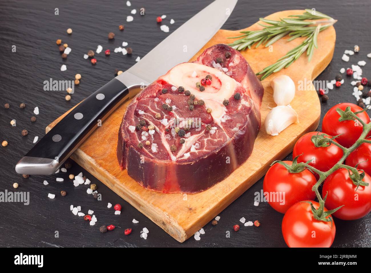 raw meat beef steak with bone, spices, rosemary and cooking ingredients on cutting board and black slate background. top view, flat lay. Stock Photo