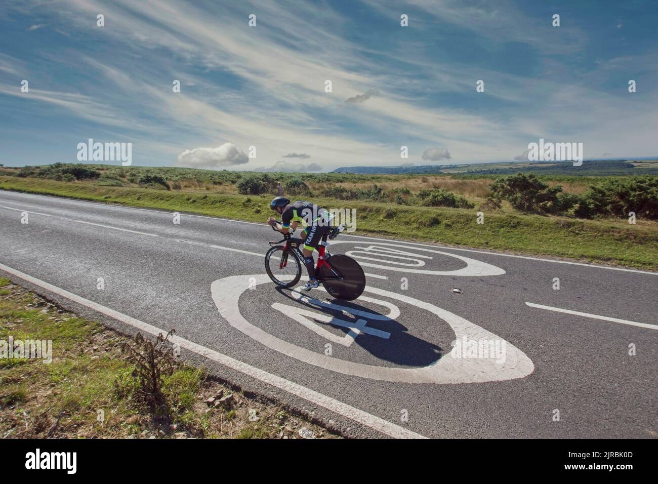 7thAug22 Gower Swansea Wales UK Triathlon Ironman cycling event Cyclist crossing road painted '40' speed limit sign Centre frame heading right to left Stock Photo