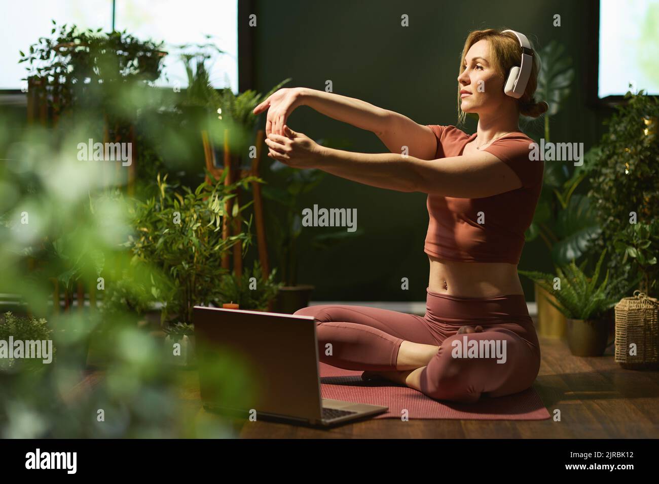 modern 30 years old housewife with laptop stretching and listening to the music with headphones in the modern green living room. Stock Photo